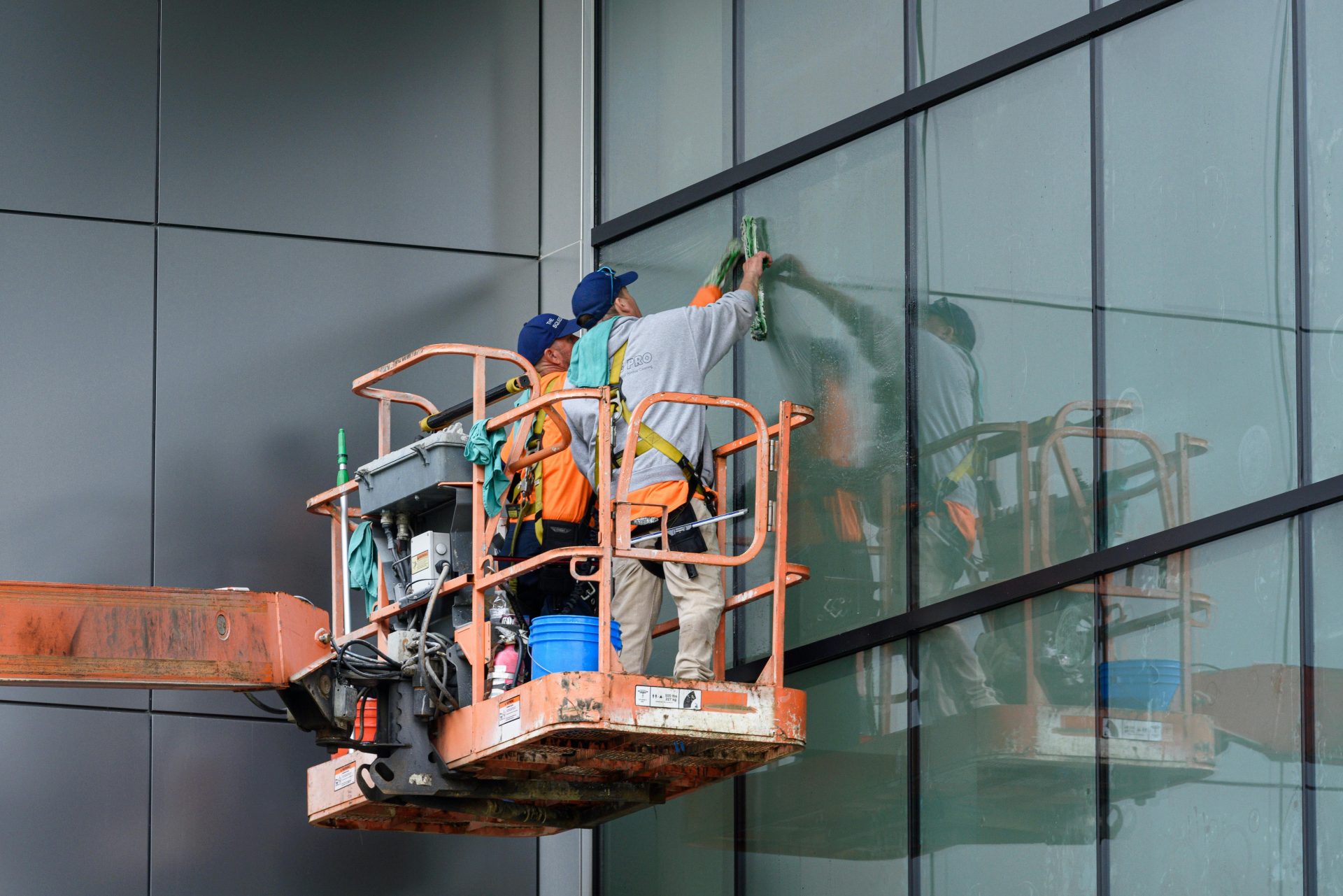 Window cleaners working on a skyscraper using a hydraulic lift in urban setting.